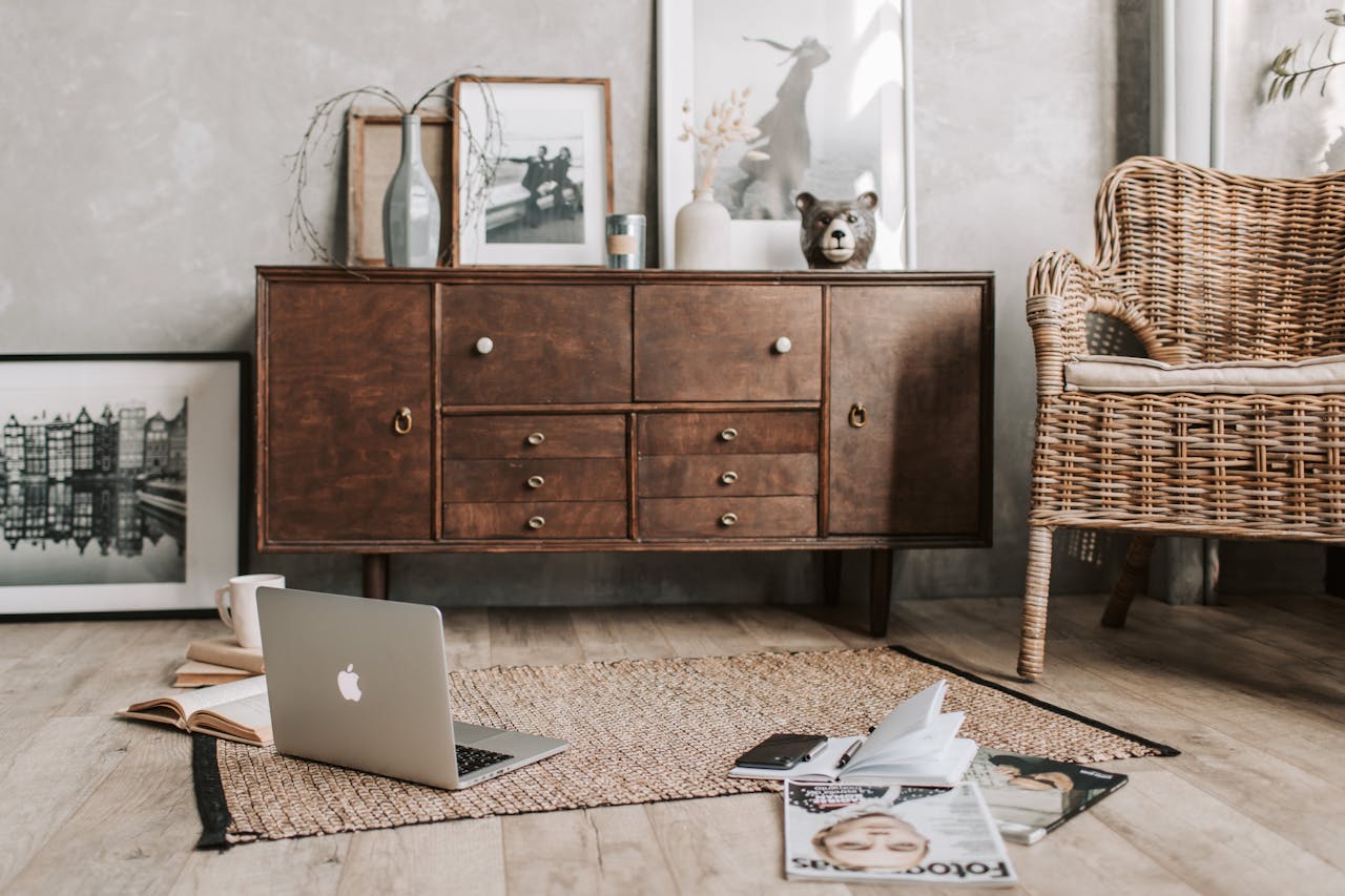 A cozy home office interior featuring a rustic wooden cabinet, wicker chair, and open laptop.